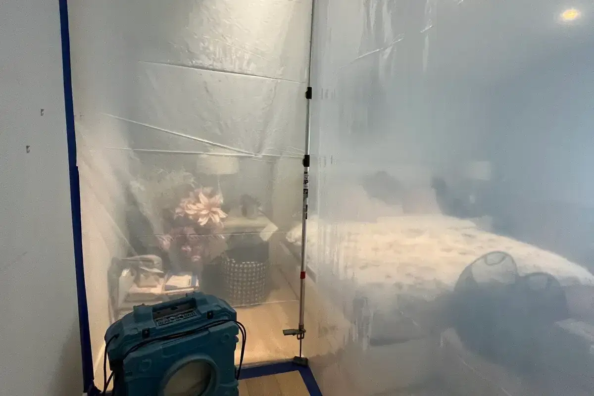 Plastic containment and a HEPA air scrubber isolating a bedroom during remediation.