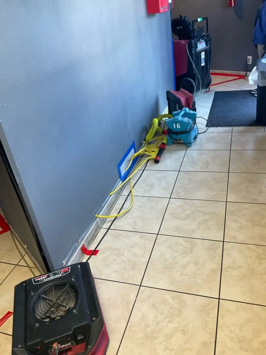 Air movers and a dehumidifier drying a tiled commercial hallway.