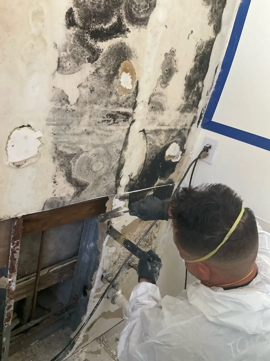 Technician in PPE removing mold-stained drywall after a flood cut.