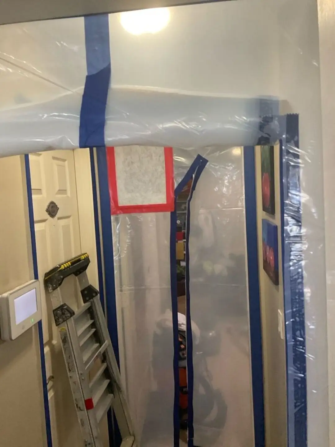 Clear plastic containment with a zipper entry and red-taped filter vent seals a hallway, with a silver ladder beside it.