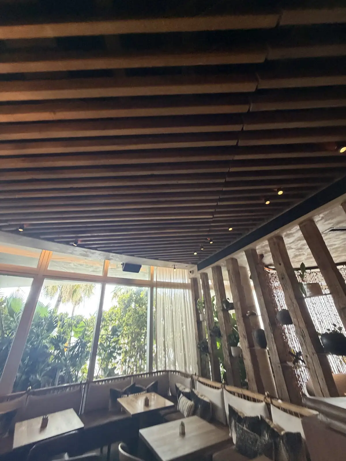 Clean dining booths, wood tables, and a wood-slat ceiling beside floor-to-ceiling windows in a Miami Beach restaurant.