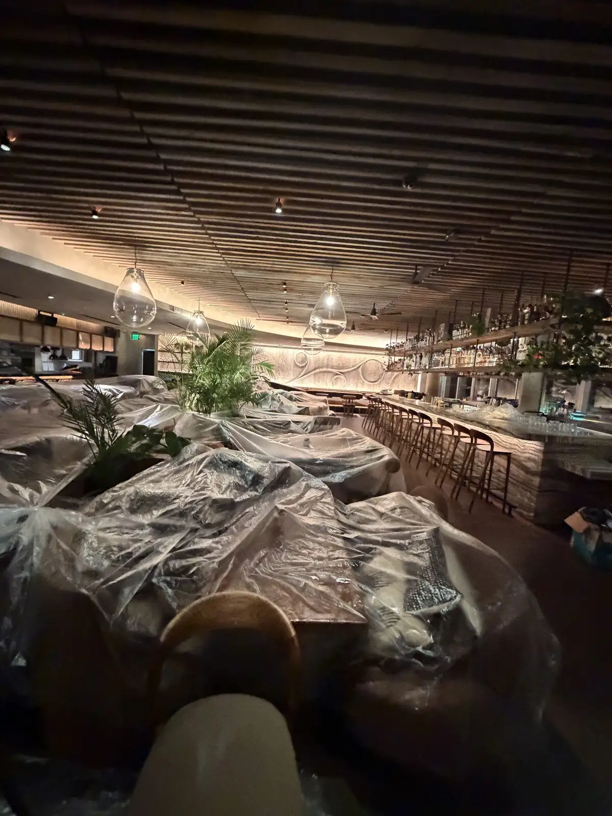 Restaurant dining tables and seating covered in clear plastic during sanitization.