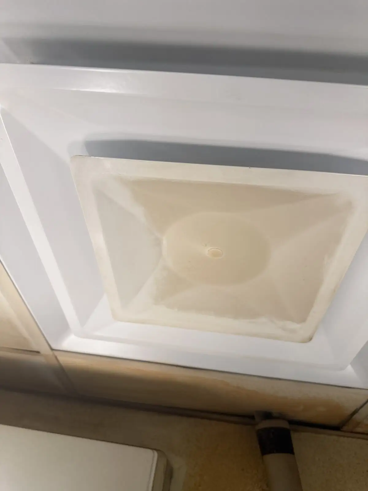 Greasy square HVAC ceiling diffuser and stained drop-ceiling tile in a commercial kitchen before sanitization.