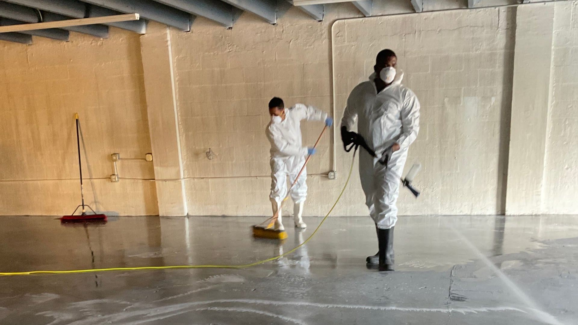 Two Total Care Restoration technicians in protective suits and respirators washing down a warehouse floor after a fire