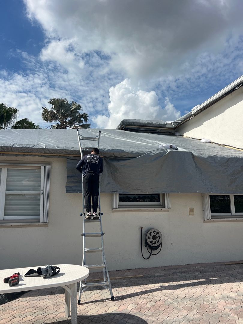 Professional grey tarp installation on damaged Florida roof for emergency storm protection